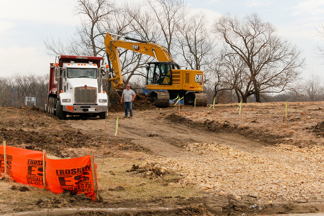 A construction worker standing next to a dump truck and a backhoe