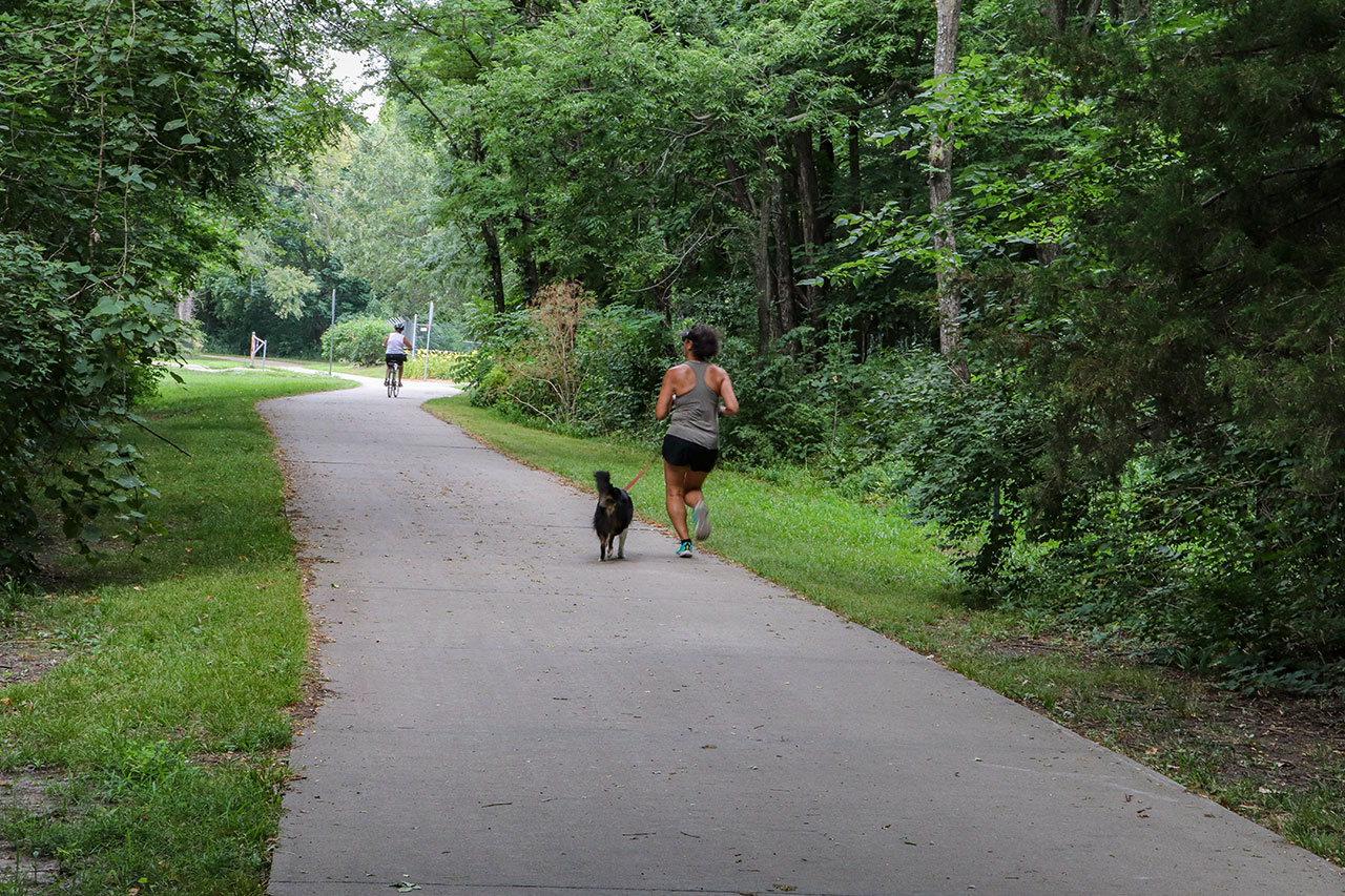 A woman running with her dog and a man on a bike in the background