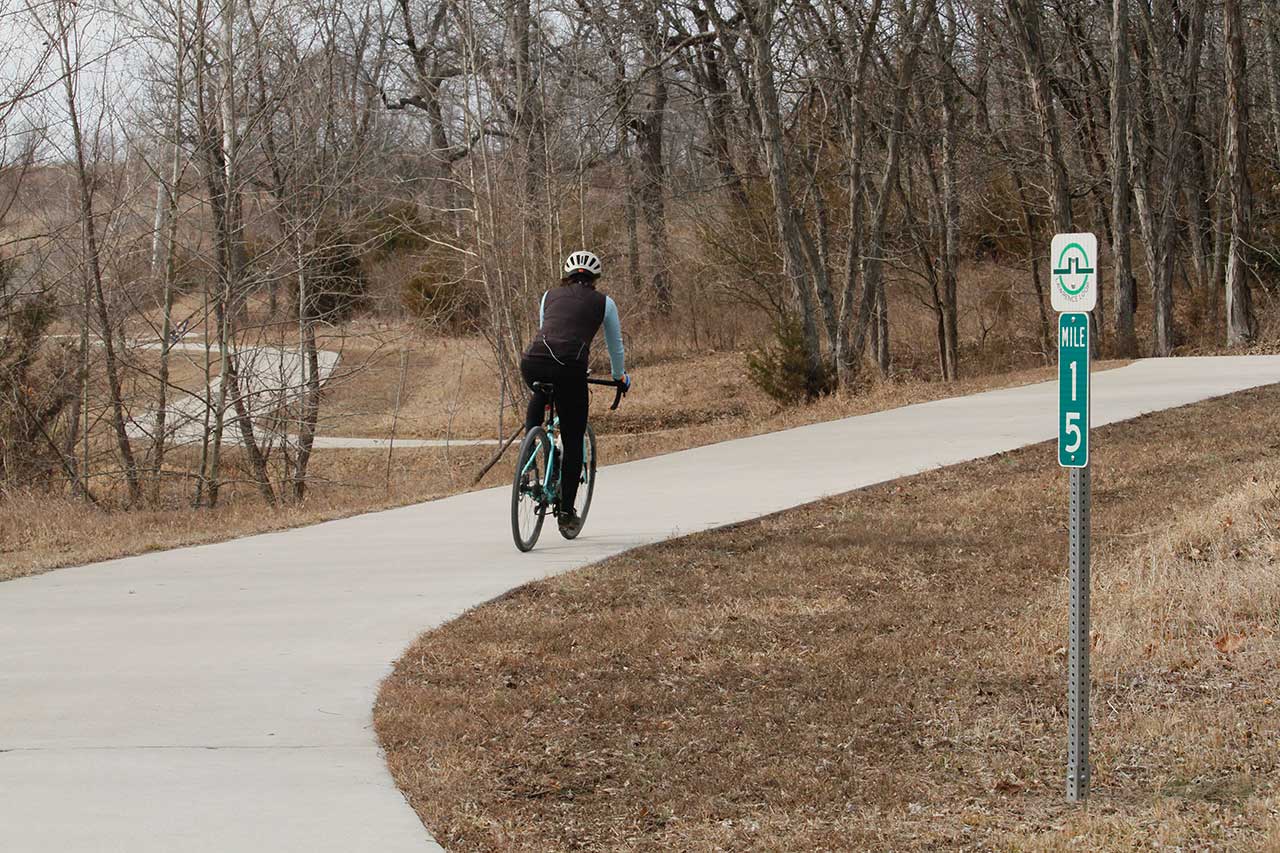 A woman biking past the mile marker 15 sign