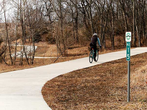 A woman biking past mile marker 15 of the Loop