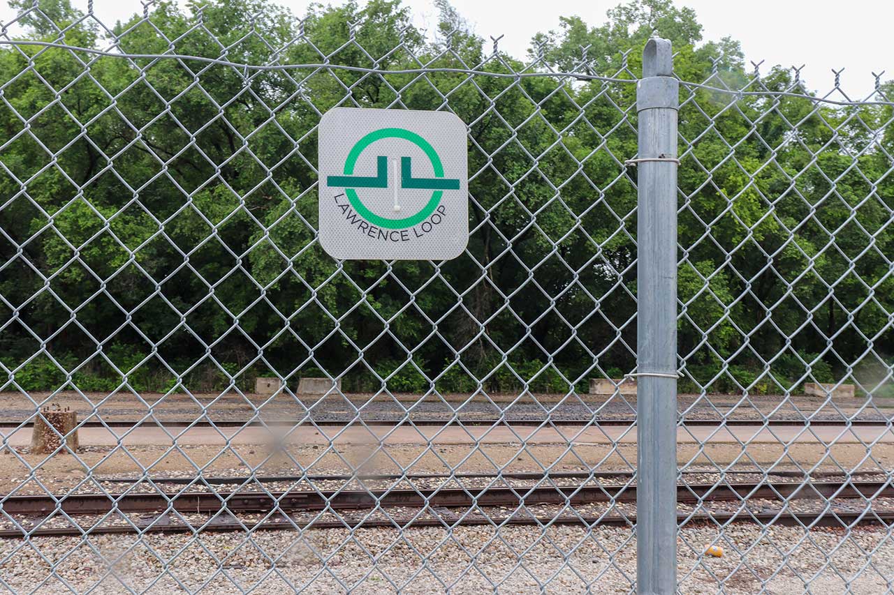 A Lawrence Loop sign on the fence along the railroad track